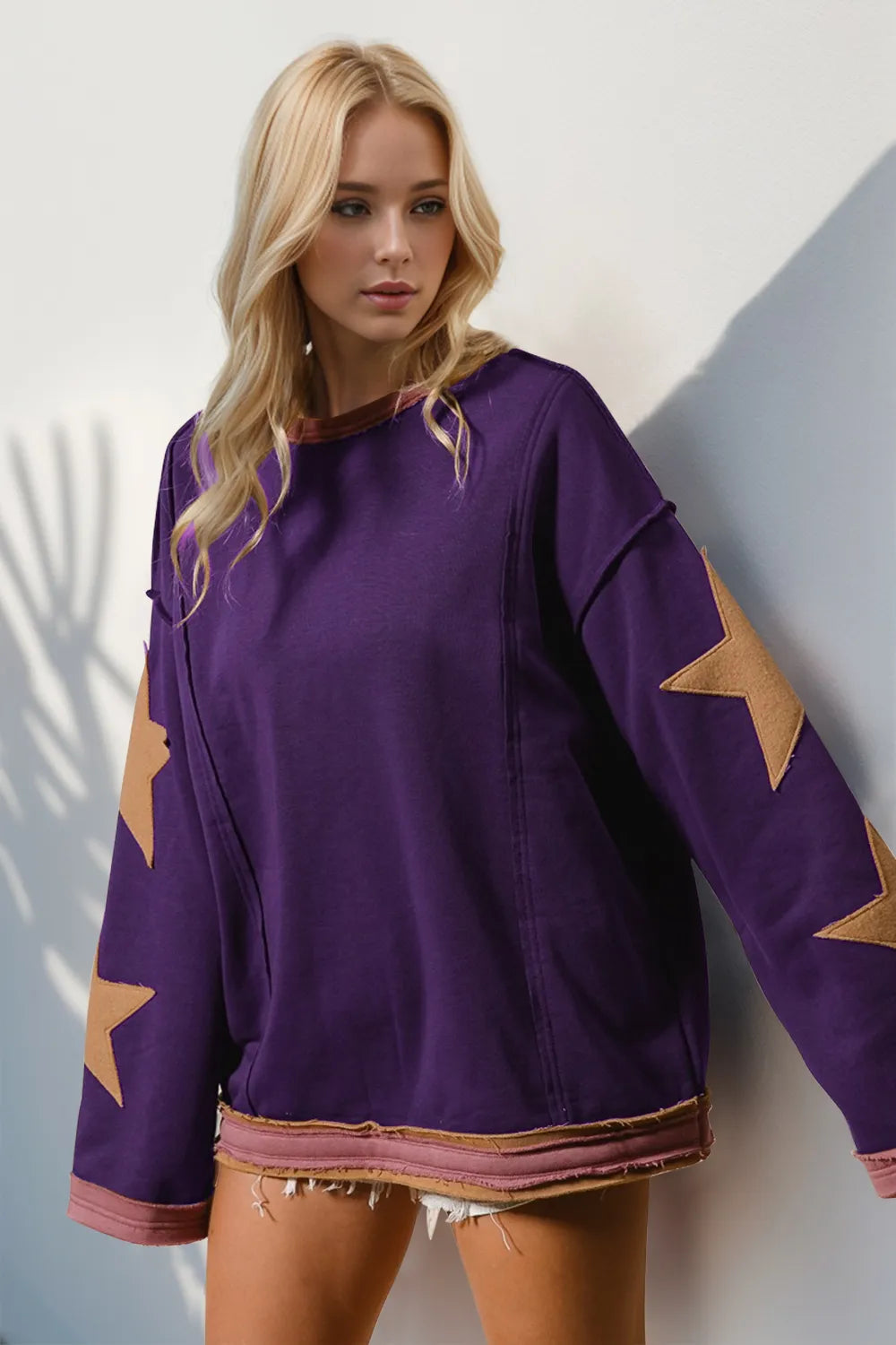 Purple long sleeve sweatshirt with orange star patches on sleeves, worn by a blonde model.