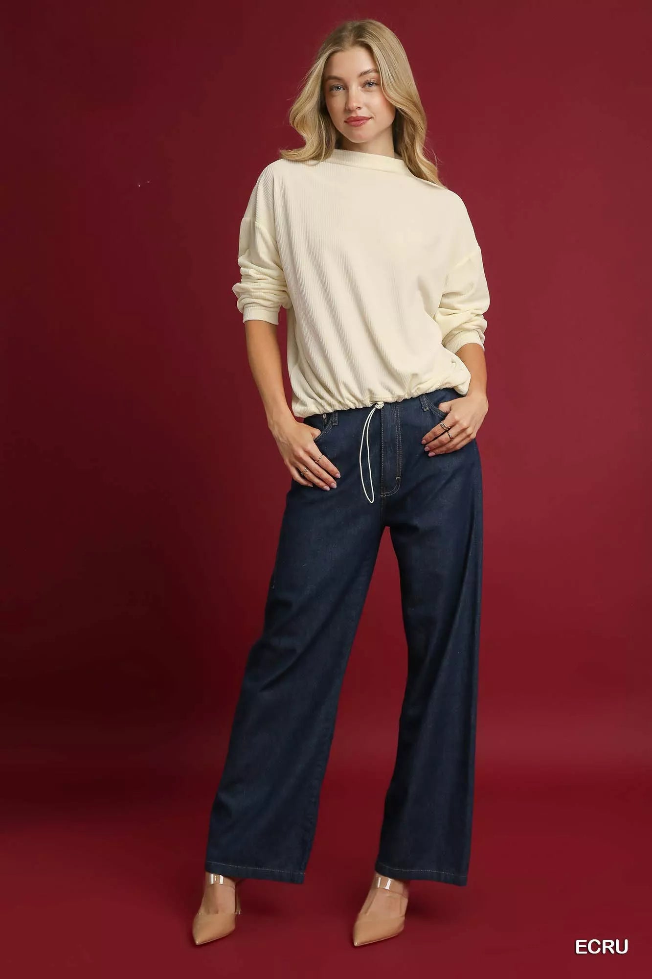 Woman wearing cream ribbed knit top with drawstring hem and wide-leg jeans.