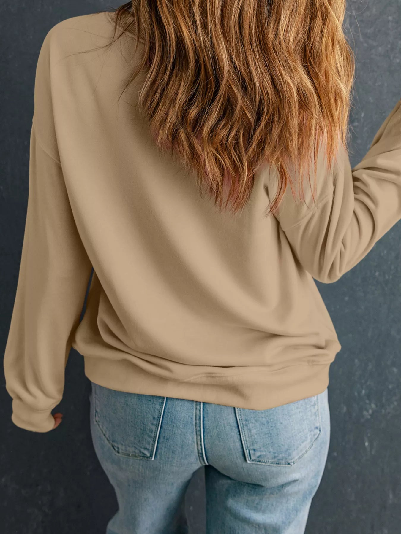 Rear view of a woman wearing a beige camouflage Thanksgiving turkey graphic sweatshirt with long sleeves.