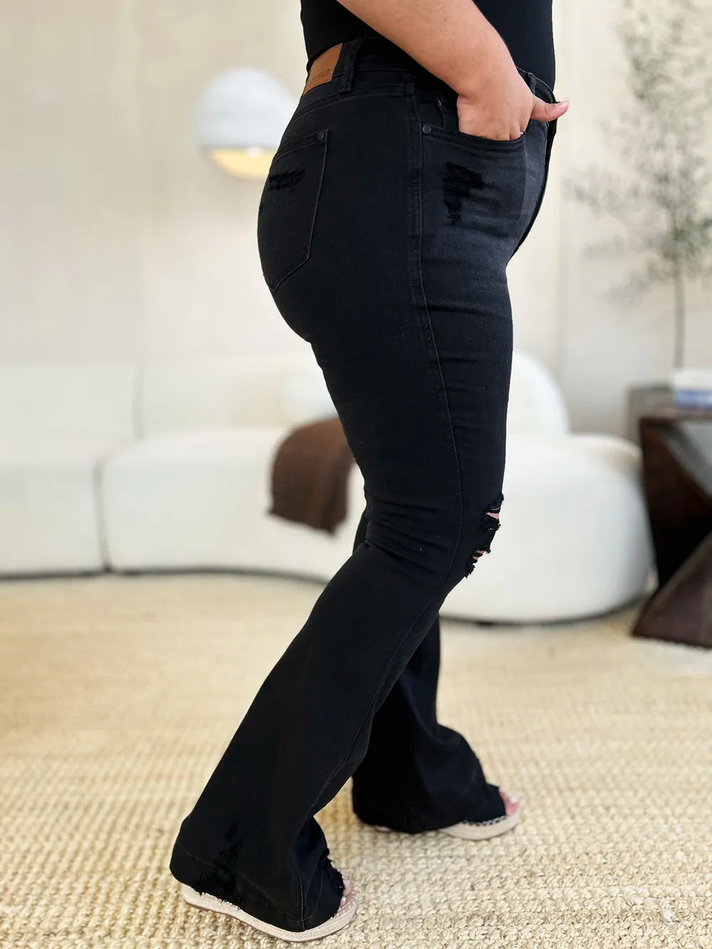 High-waist black distressed flare jeans modeled on a curvy woman.