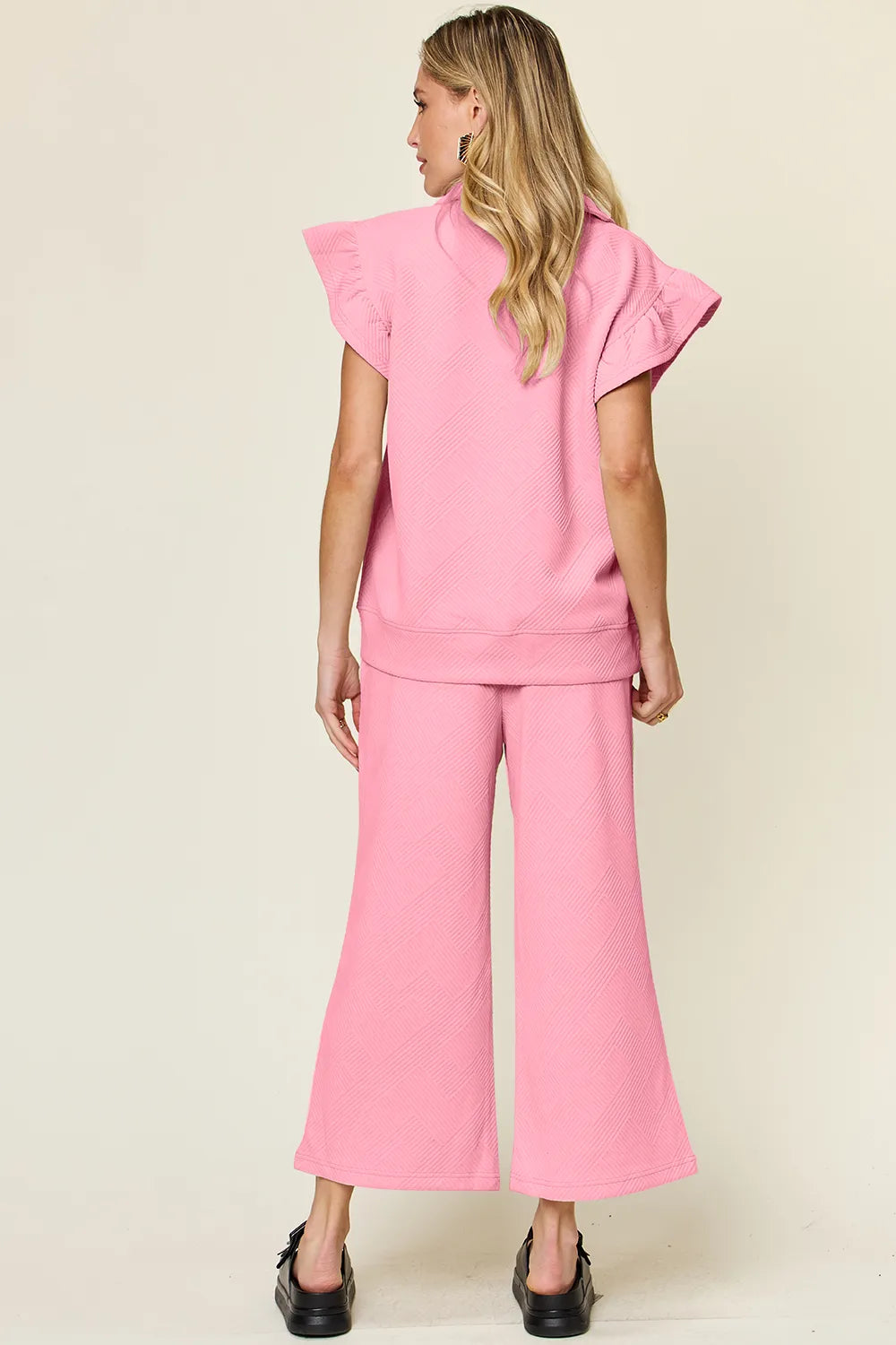 Rear view of a woman modeling a pink textured ruffle short sleeve top and wide leg pants set.