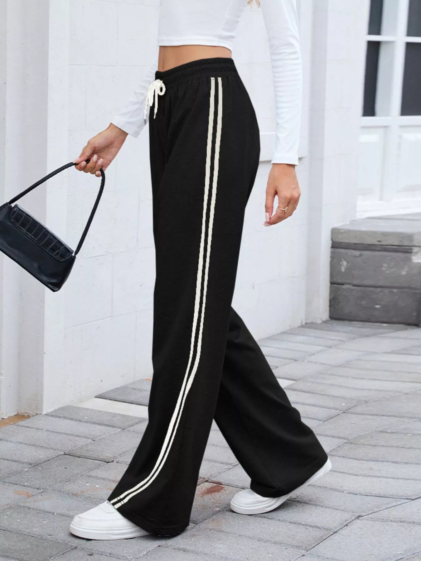 Black side striped wide leg pants with drawstring waist, modeled on a person outdoors.