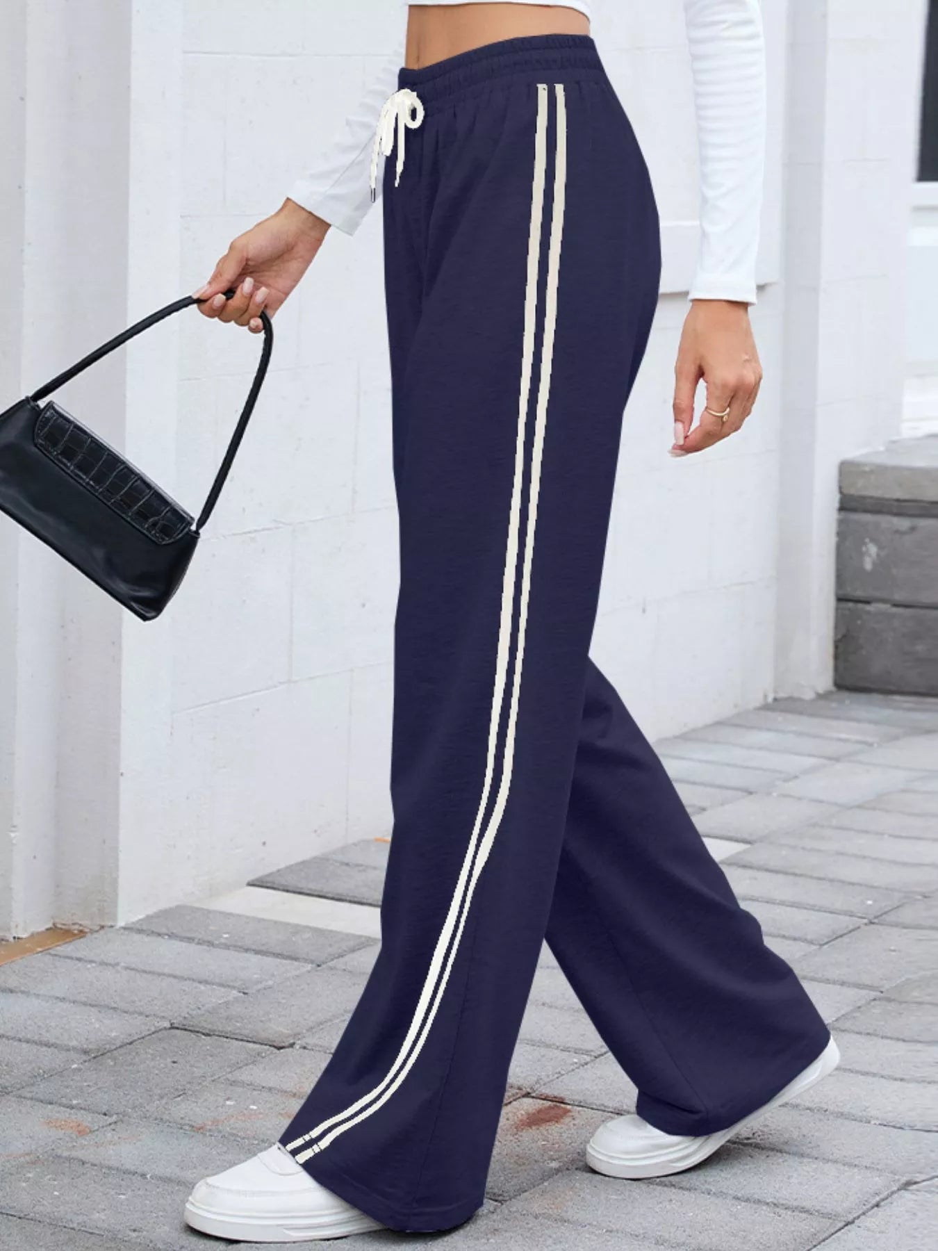 Model wearing navy side-striped wide-leg pants with drawstring waist and white sneakers.