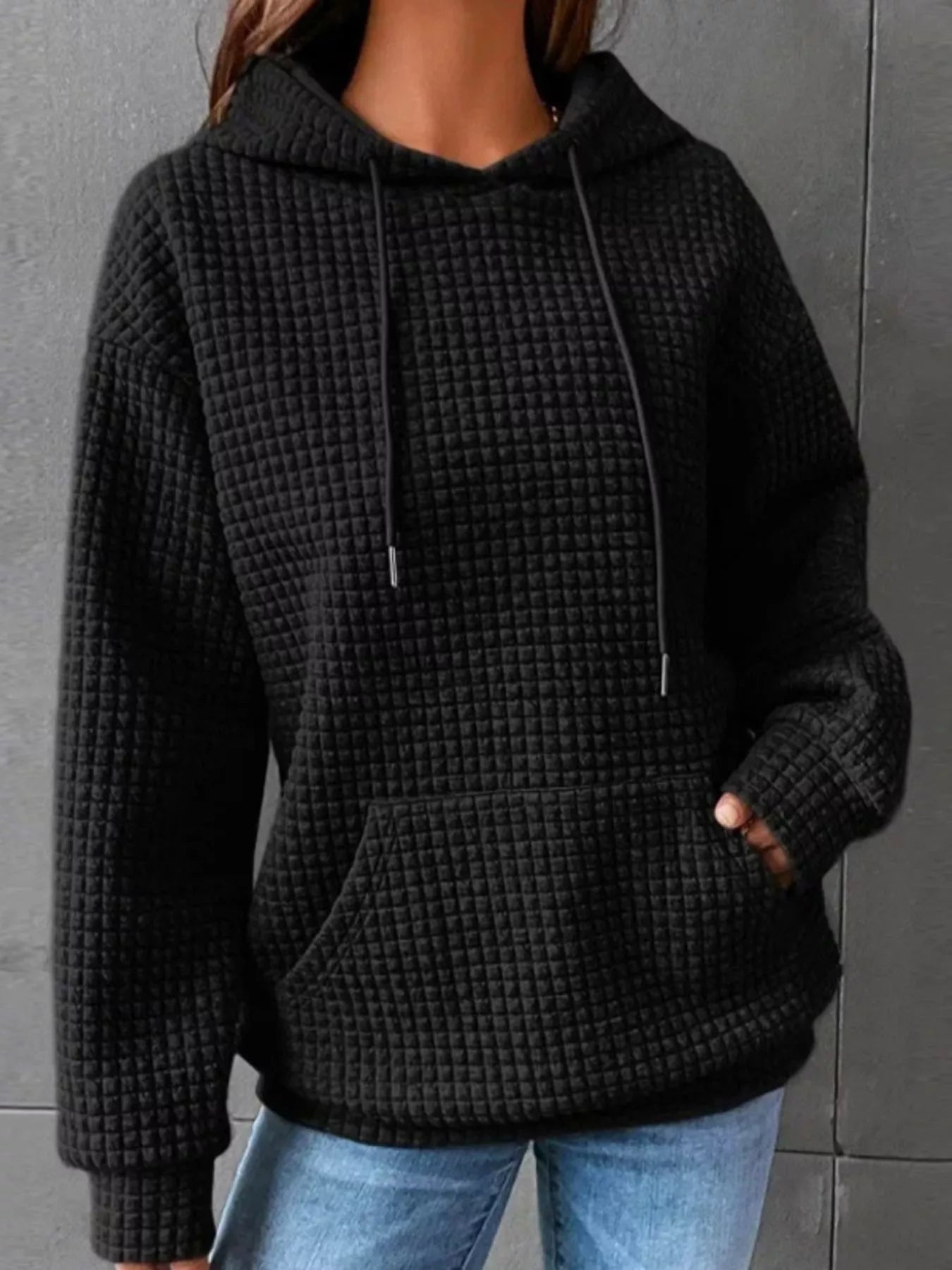 Black waffle knit hoodie with drawstring hood and front pocket, worn by a model.