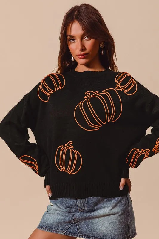 Black knit Halloween sweater with orange embroidered pumpkins, modeled on a woman.
