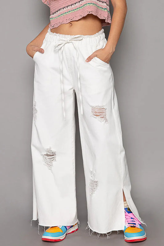 White distressed drawstring wide-leg cotton pants with pockets and side slits, modeled on a woman.