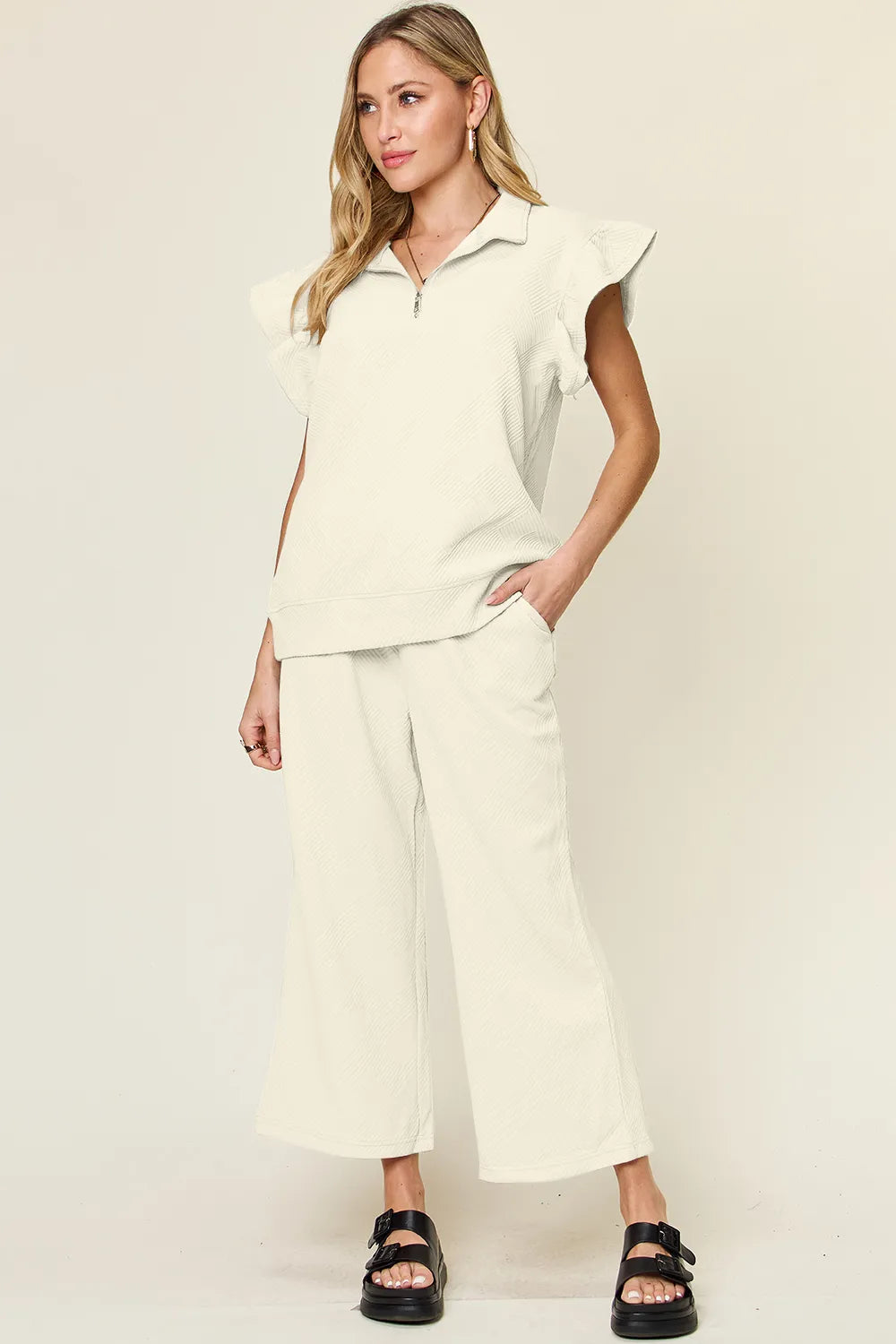 Woman modeling a white textured ruffle short sleeve top and wide leg pants set.