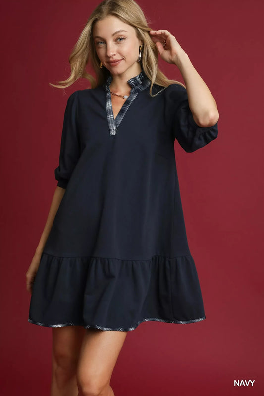 Woman modeling navy French terry ruffle hem dress with plaid trim.