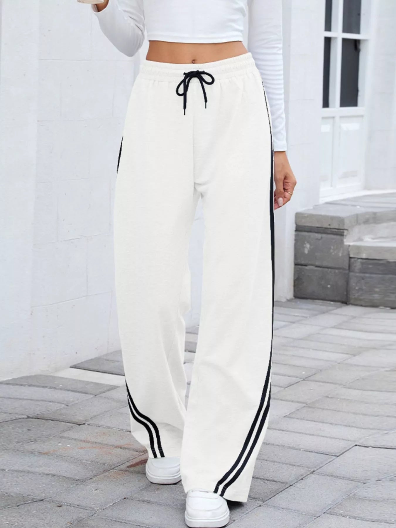 Woman wearing white wide-leg pants with black side stripes and drawstring waist.