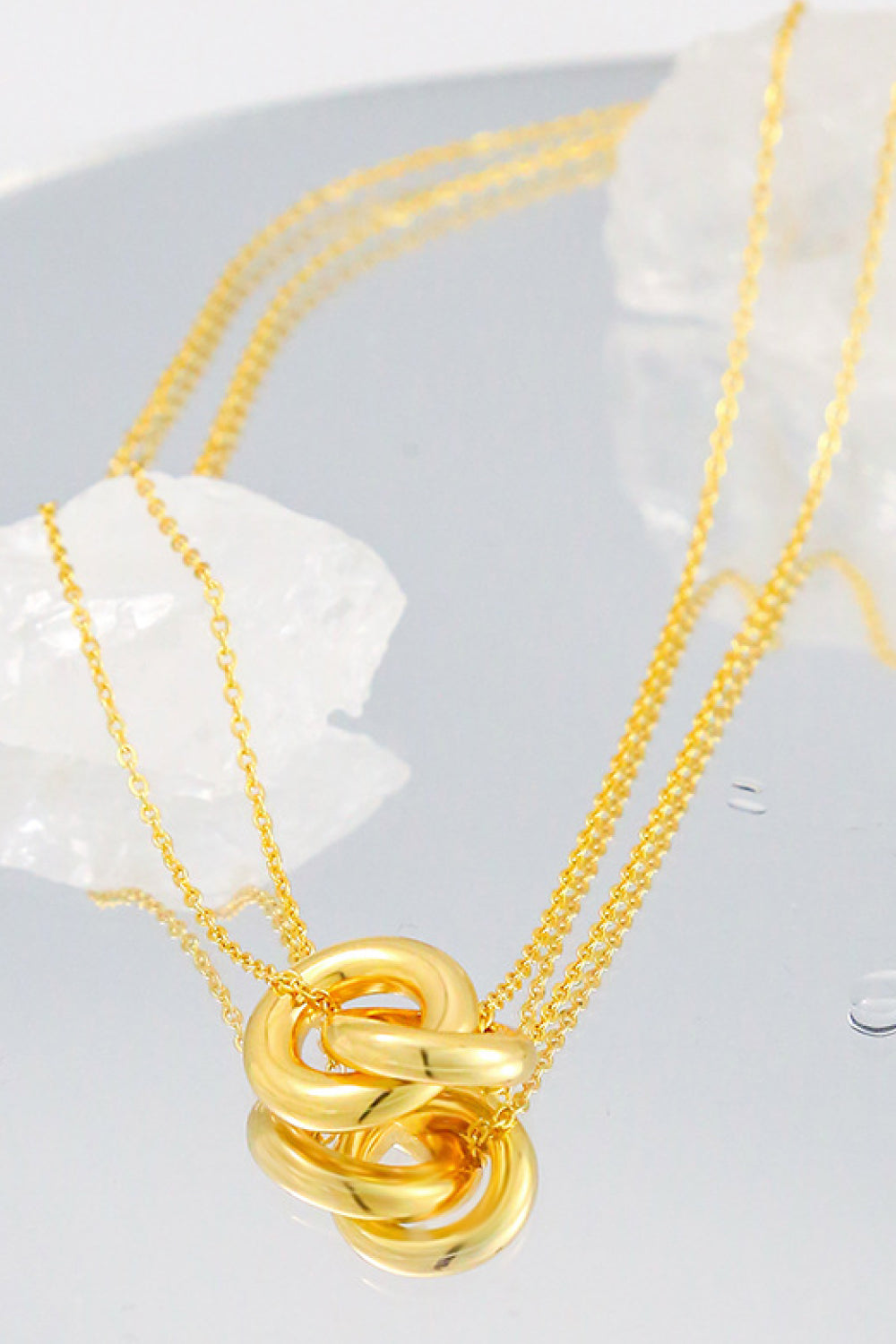 Golden brass linked ring pendant necklace on a chain, displayed on a reflective surface with white crystals.