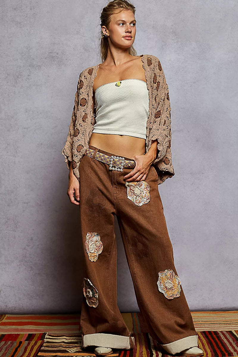 Woman wearing openwork V-neck chenille cardigan with floral contrast over white top and wide-leg pants.