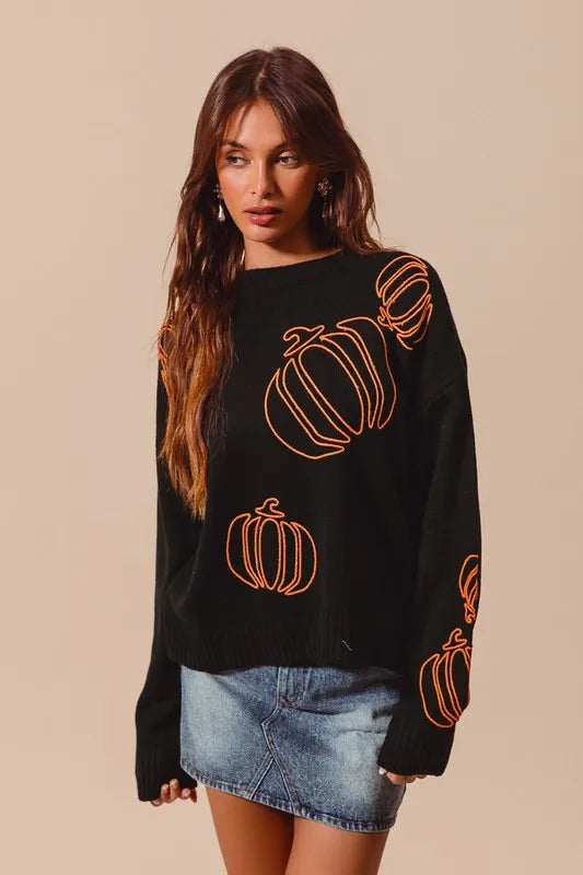 Black sweater with orange embroidered pumpkins, worn by model with long hair and denim skirt.