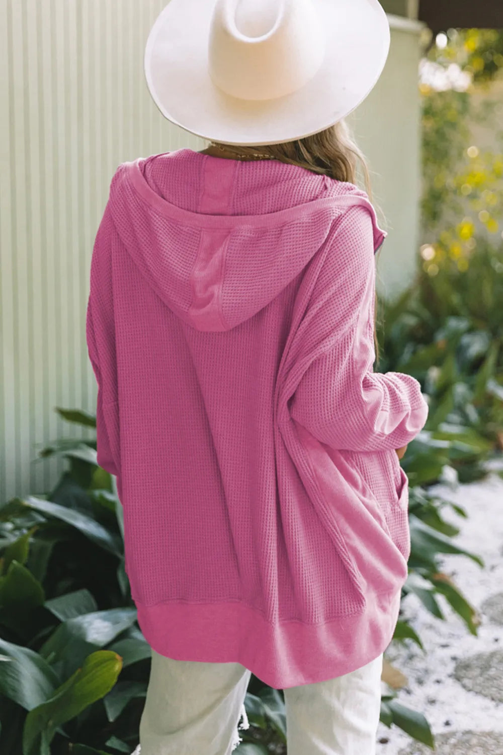Rear view of a soft pink waffle-knit zip-up hooded jacket on a model wearing a white hat.