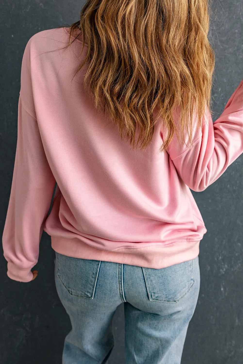 Back view of a woman wearing a pink round neck long sleeve sweatshirt with jeans.