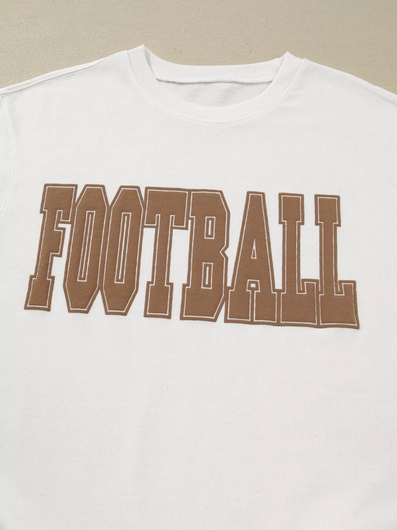 White crew neck sweatshirt with brown 3D "Football" graphic print.