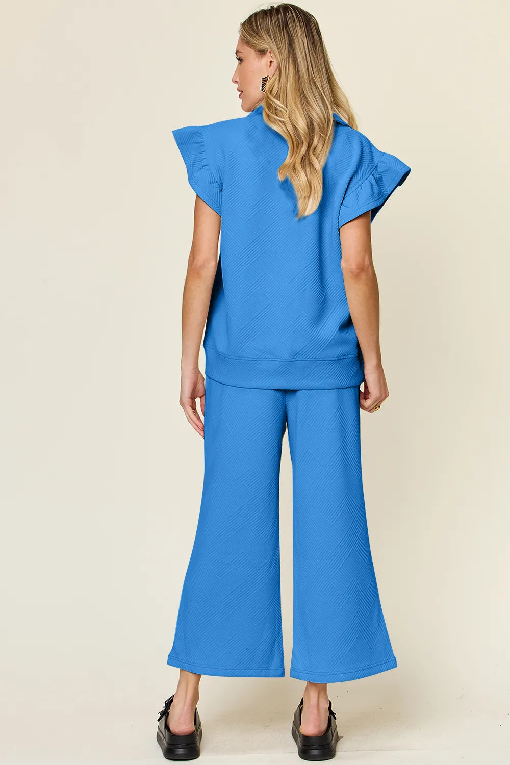 Rear view of a woman in a textured blue ruffle short sleeve top and wide leg pants set.