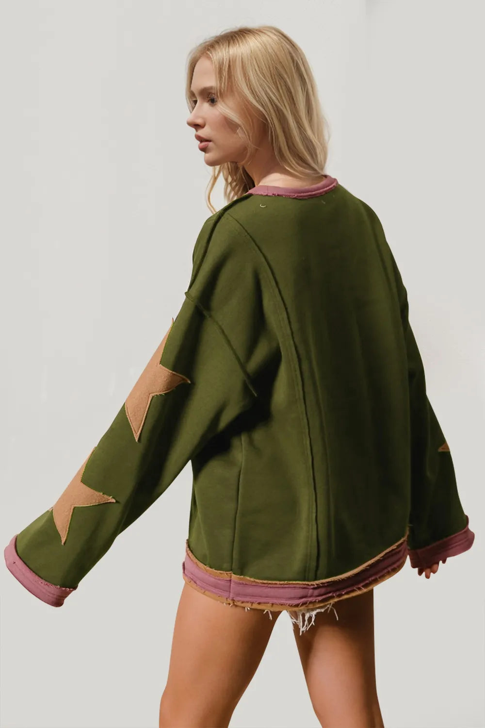 Back view of green long-sleeve sweatshirt with star patches on sleeves and pink trim.