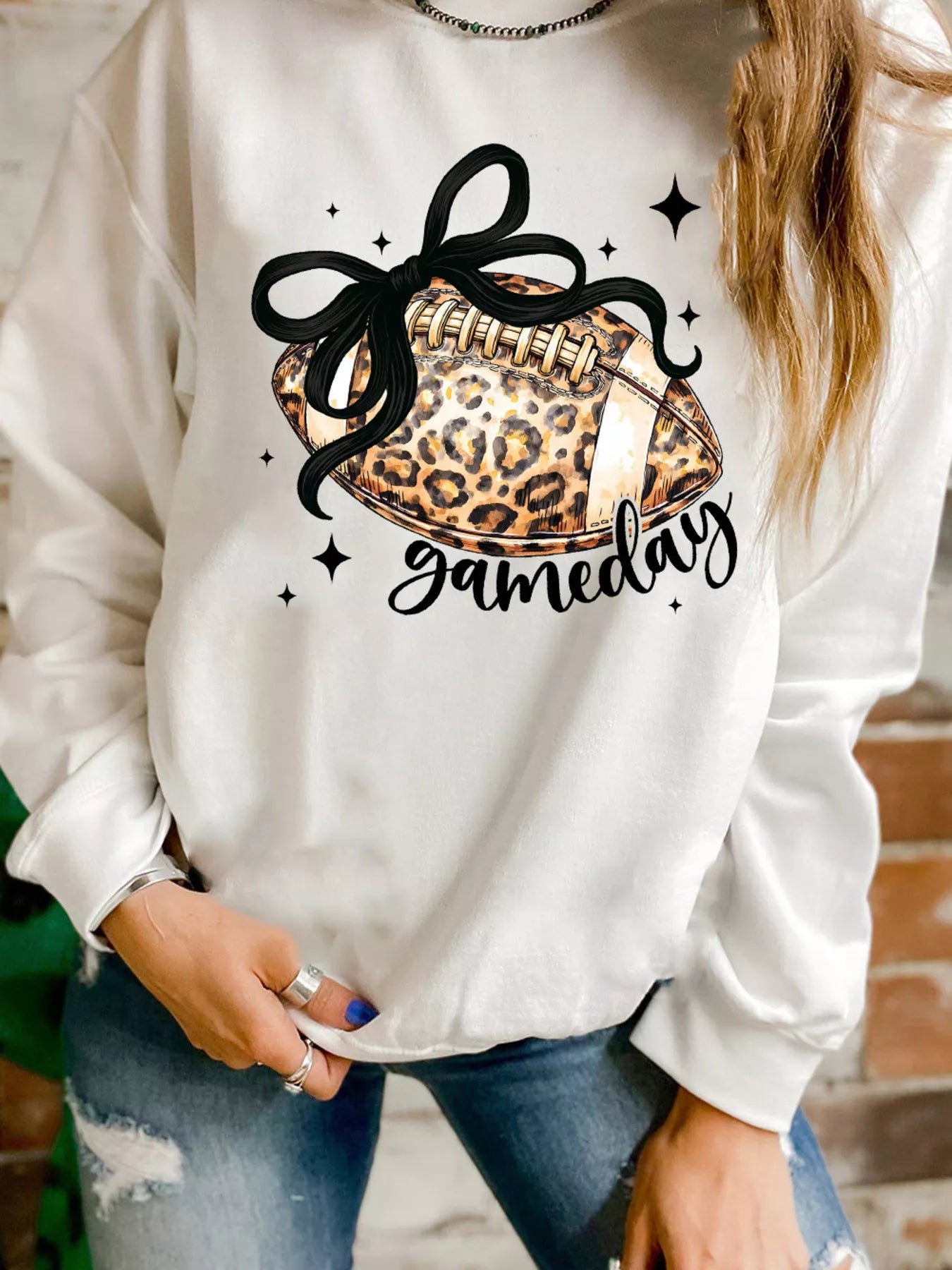 White crew neck sweatshirt with black football and leopard print graphic and "gameday" text.