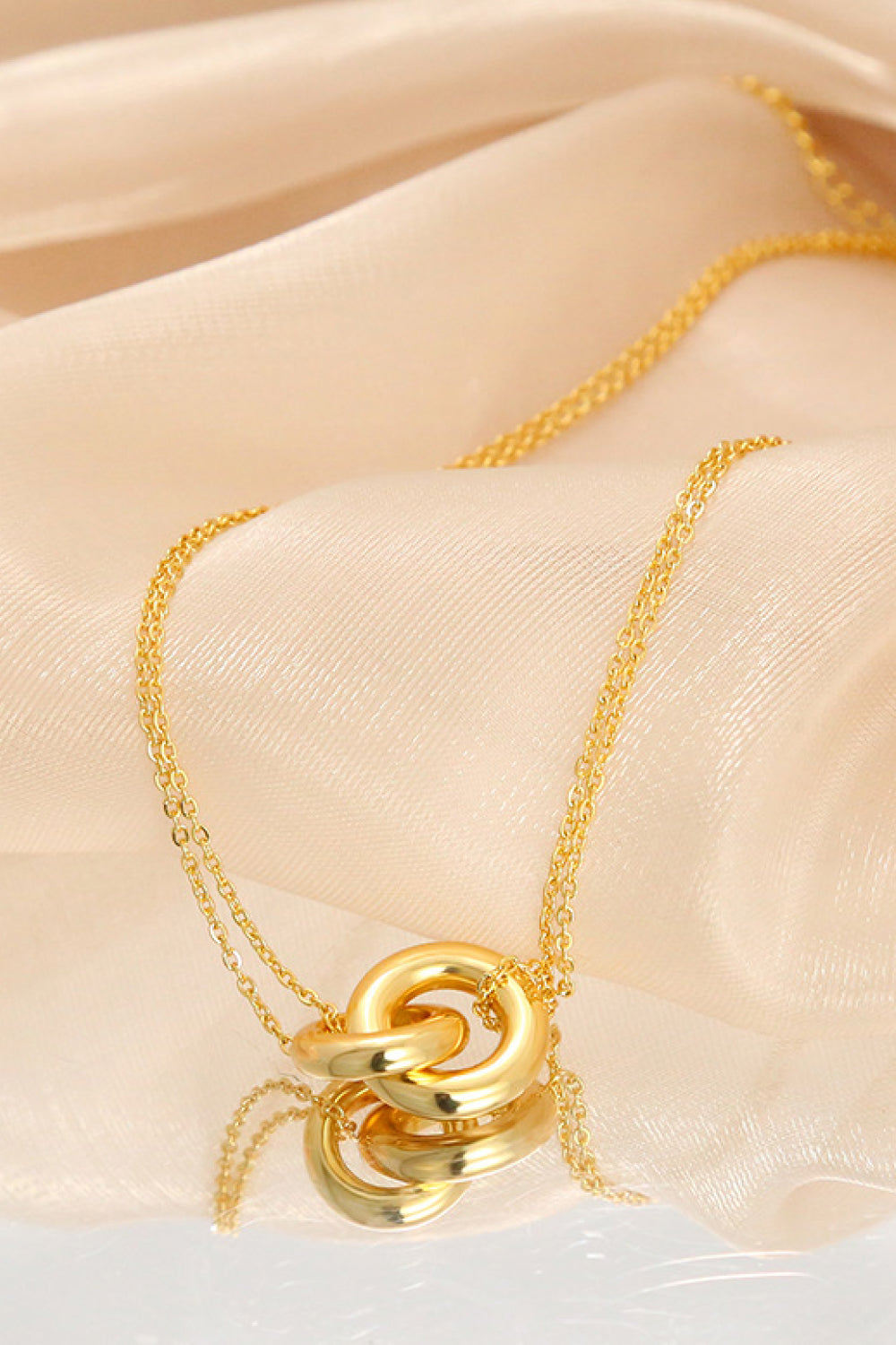 Golden brass linked ring pendant necklace on a delicate chain, laid flat on beige fabric.