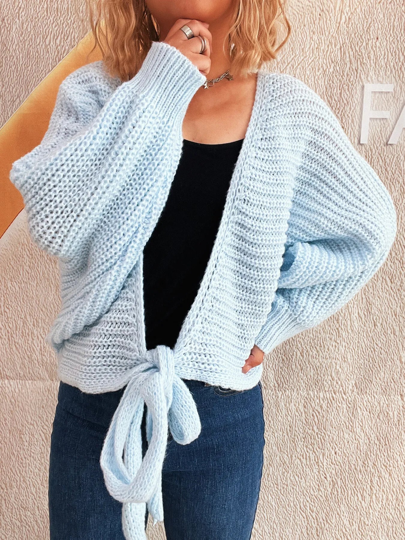 Light blue long-sleeve cardigan with tie front, worn open over black top and jeans.