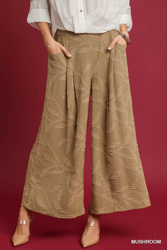 Wide-leg jacquard pants in beige polyester with leaf patterns and pockets, model in white blouse.