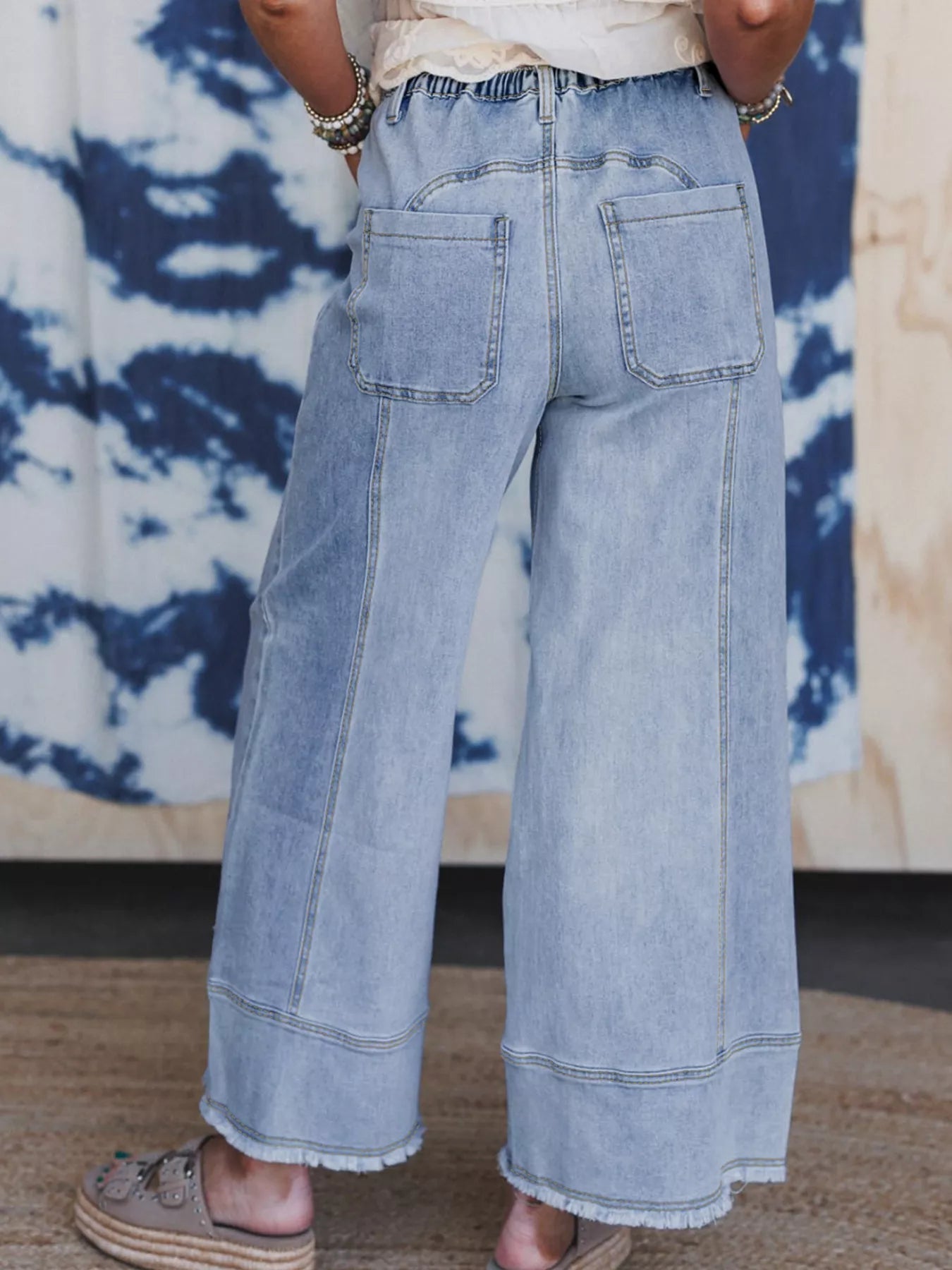 Rear view of light wash wide-leg drawstring jeans with raw hem and pockets.
