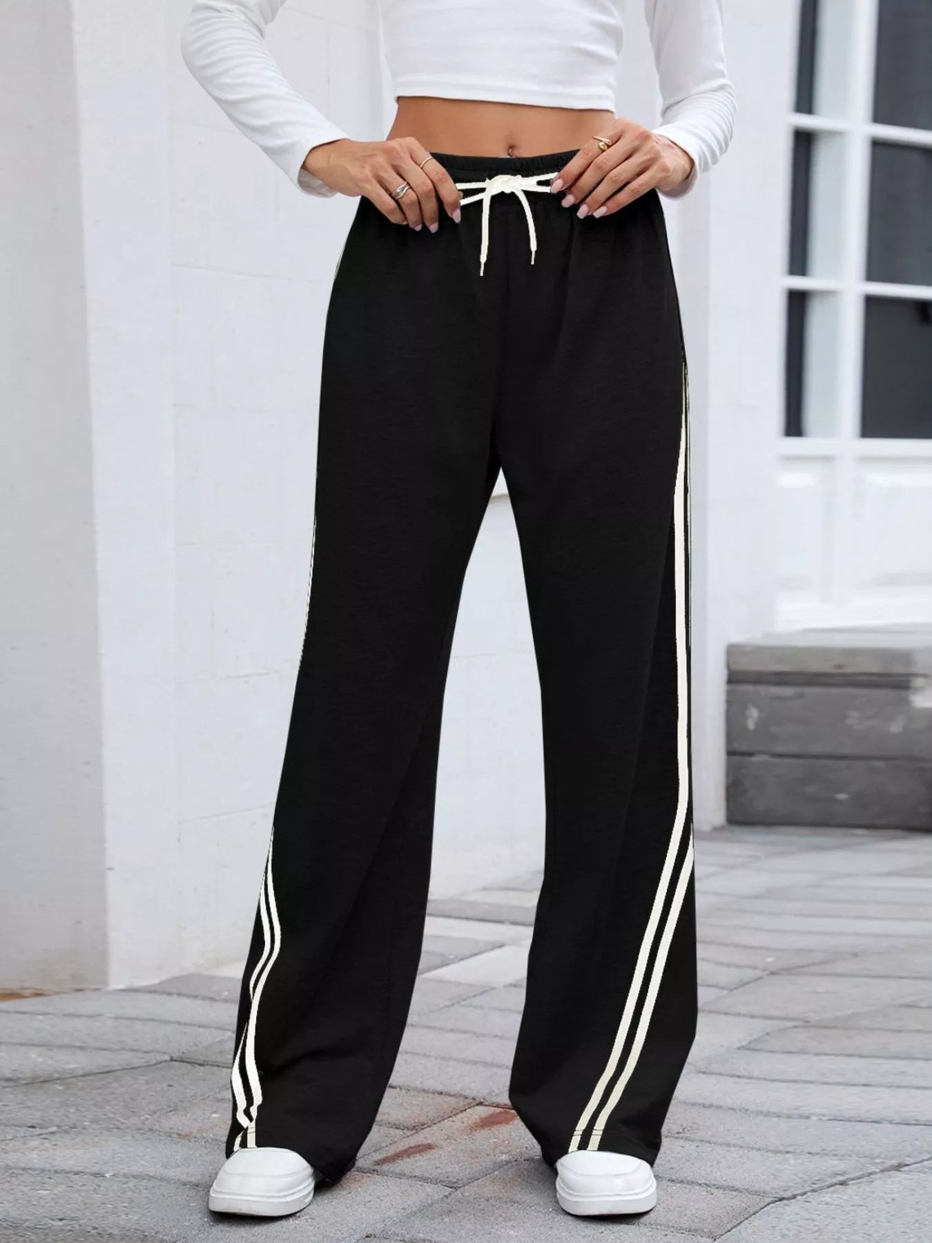 Black rayon blend wide leg pants with white side stripes and drawstring waist, modeled on a woman.