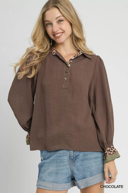 Woman modeling brown half-button blouse with leopard print trim on cuffs.