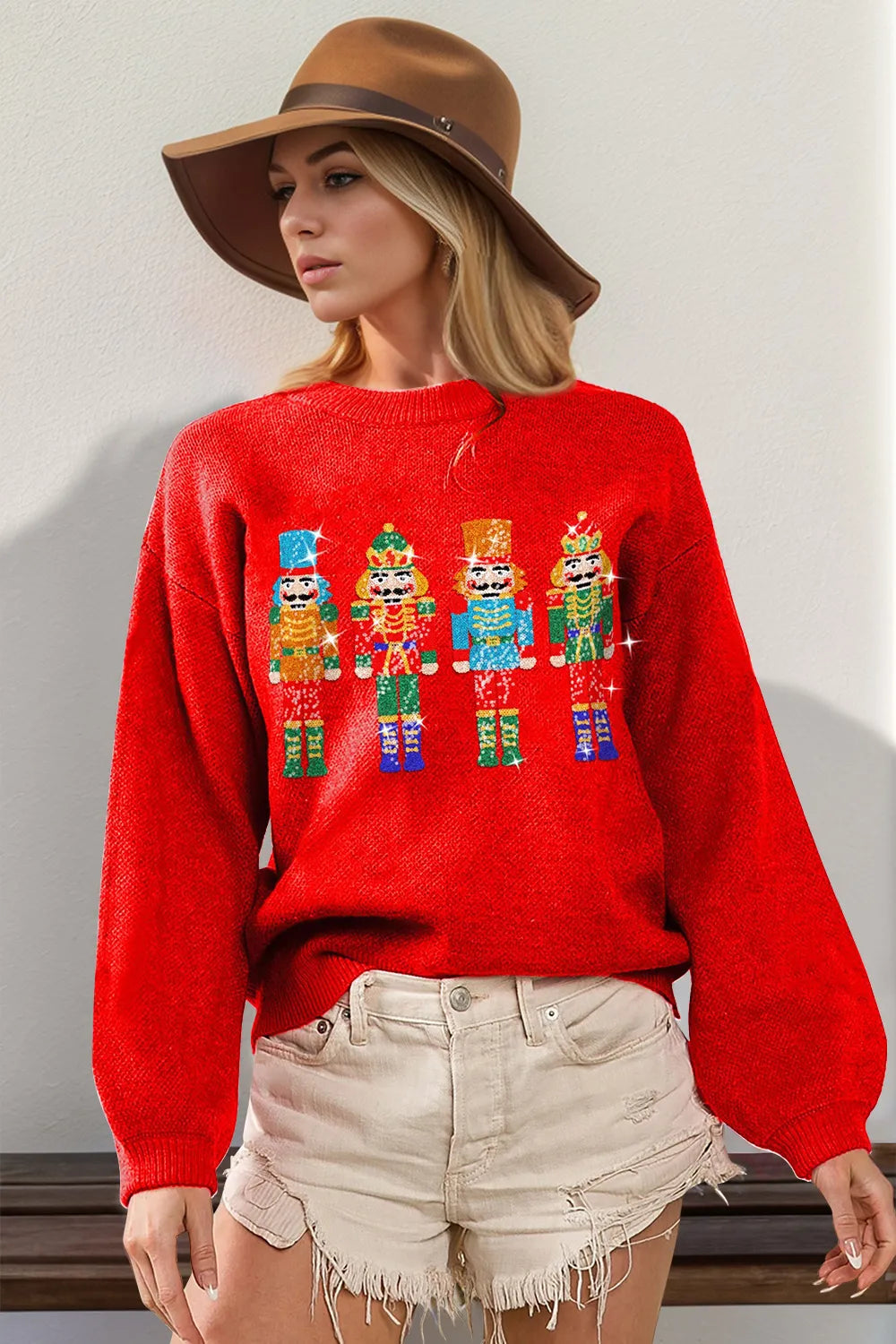 Red long-sleeve sweater with colorful sequin nutcracker designs, worn with shorts and hat.