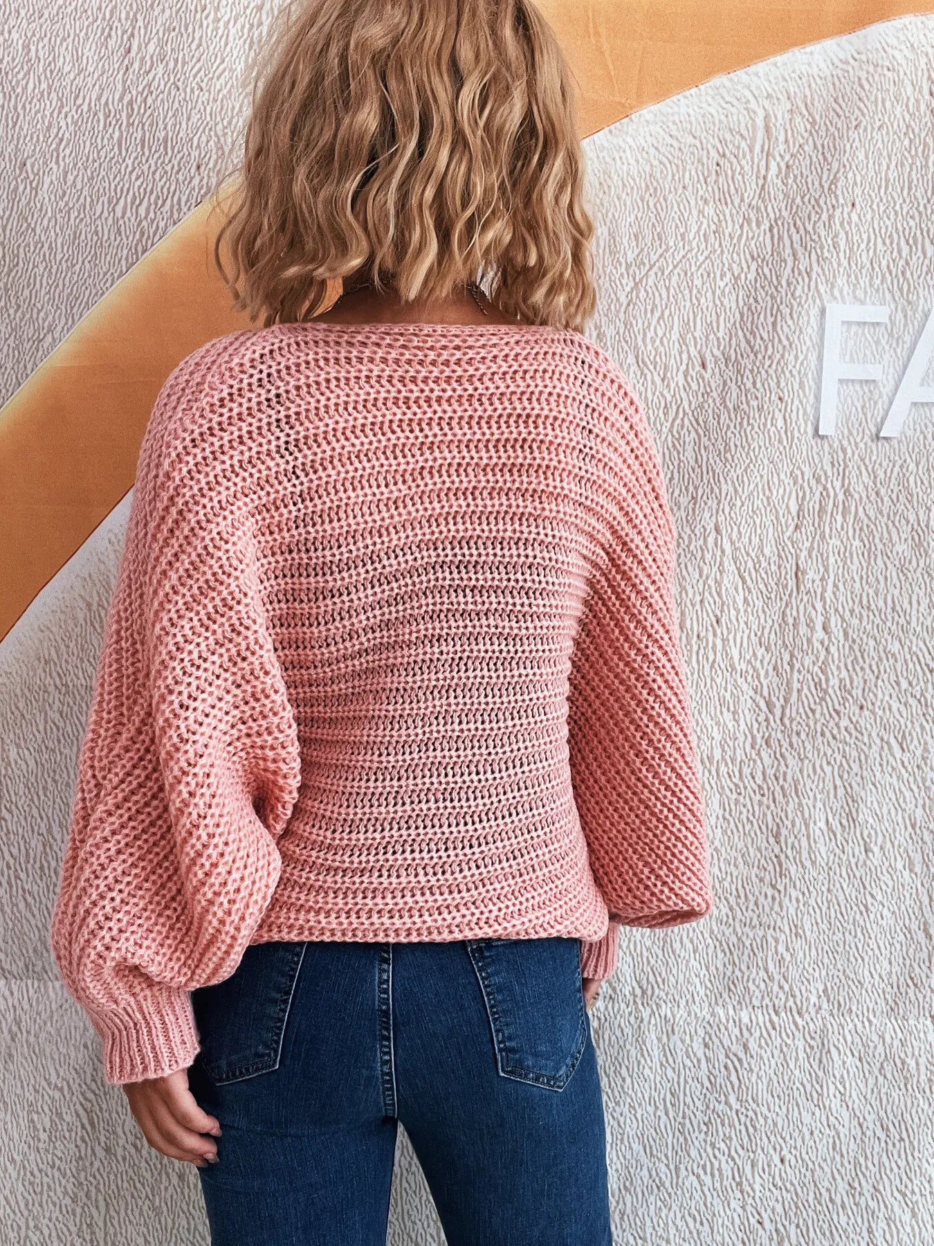 Back view of a pink open-knit cardigan with batwing sleeves on a model.