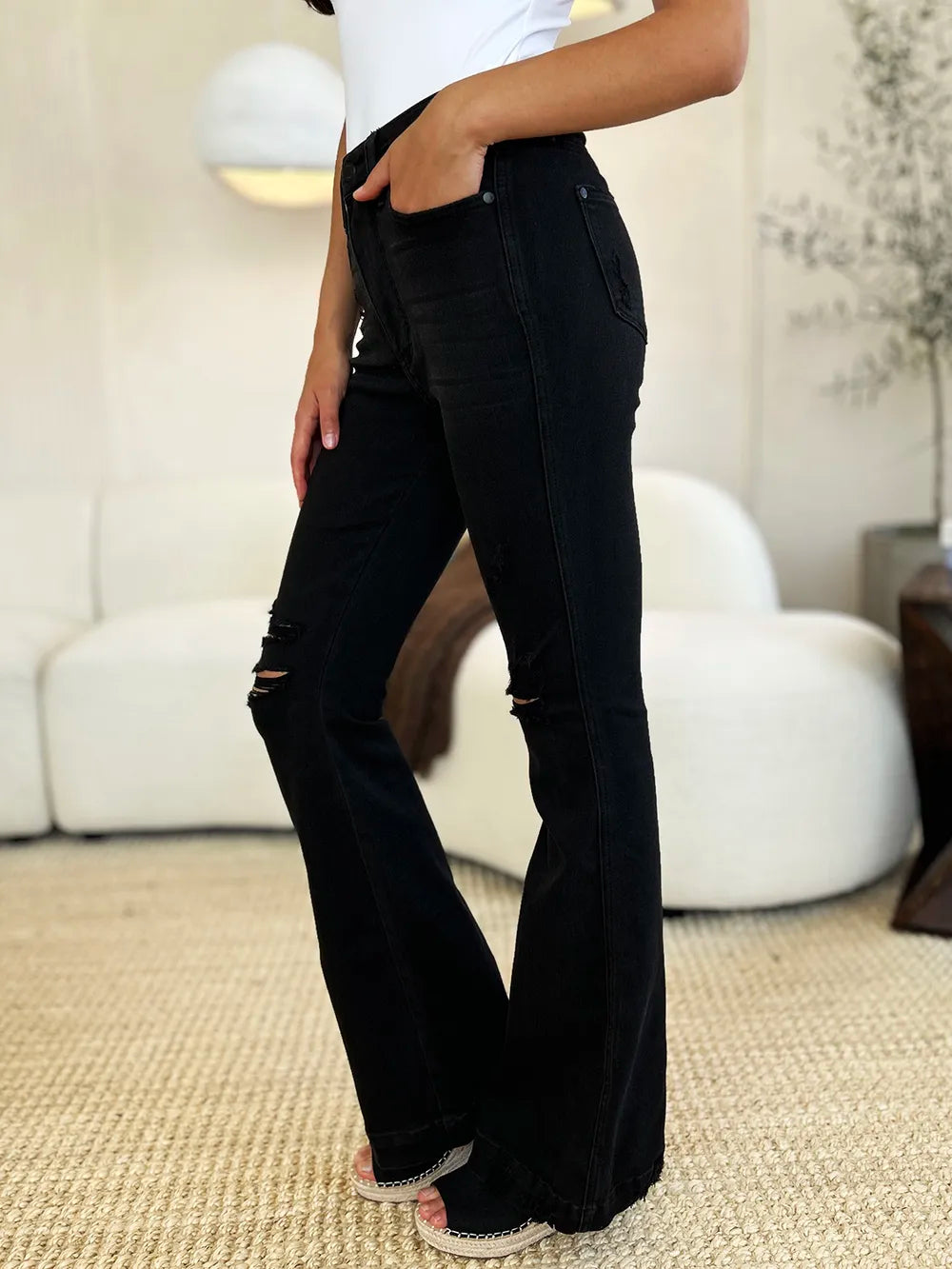Model wearing Judy Blue high-waist black distressed flare jeans with rips on legs.