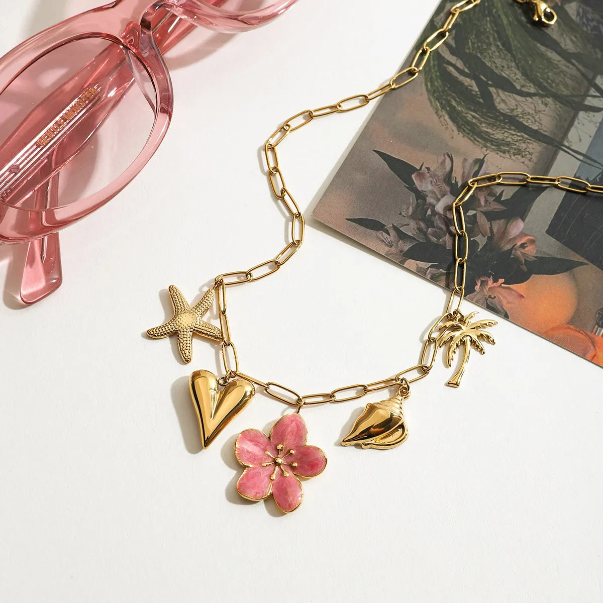 Gold-toned chain necklace with pink resin flower, starfish, heart, palm, and shell pendants.