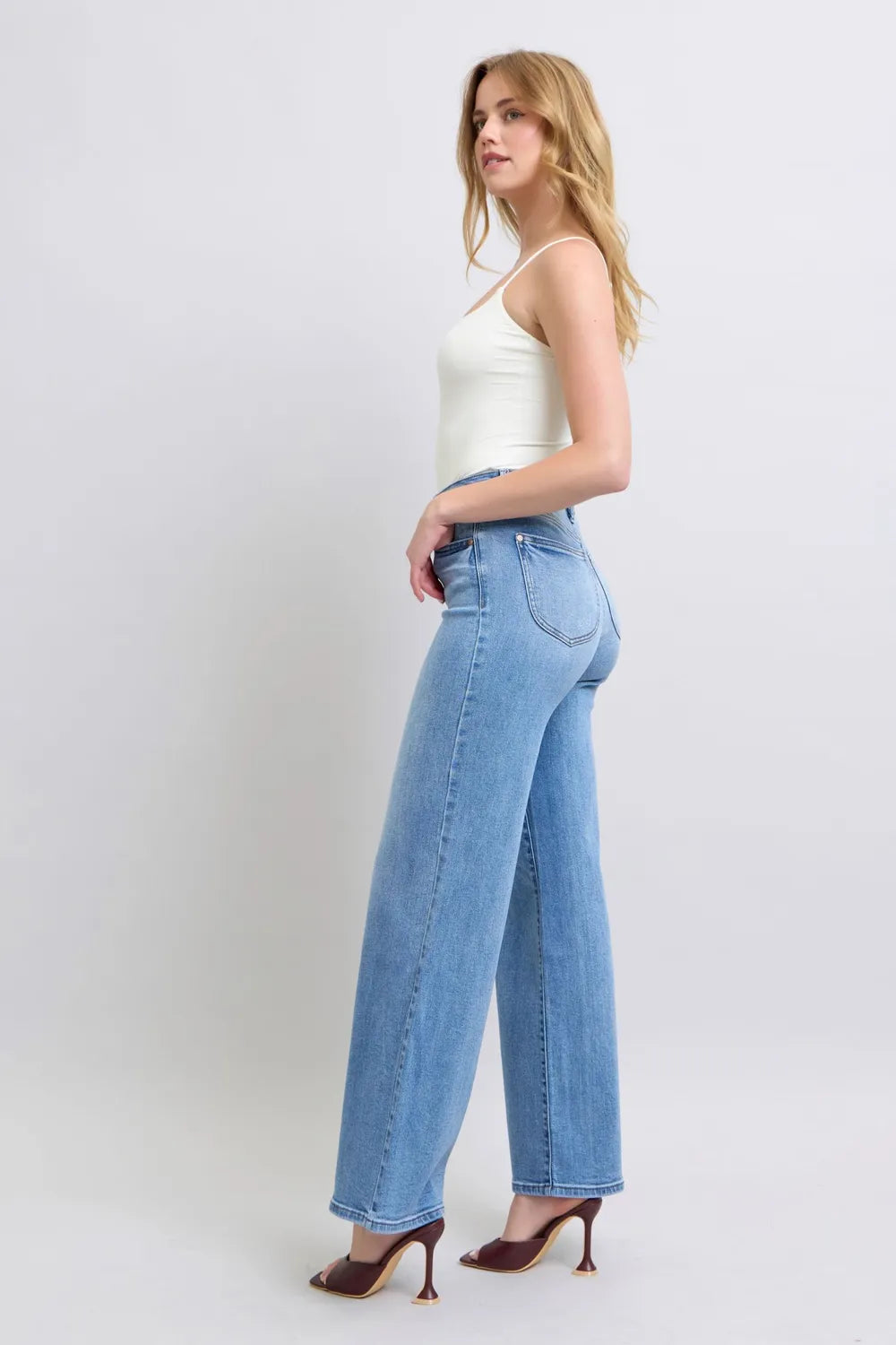 Model poses sideways in Judy Blue high-waist wide-leg jeans with pockets, cream tank top, and strappy heels.