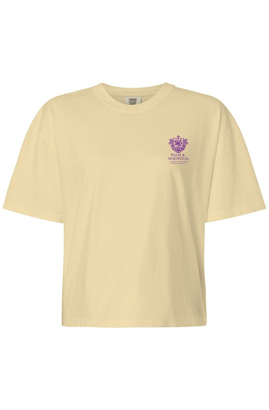 Women's boxy short-sleeve T-shirt in beige with purple crest logo on chest.