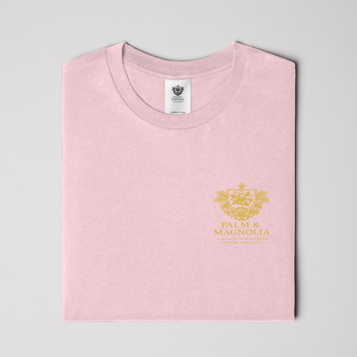 Folded pink unisex ring-spun cotton tee with gold Palm & Magnolia logo.