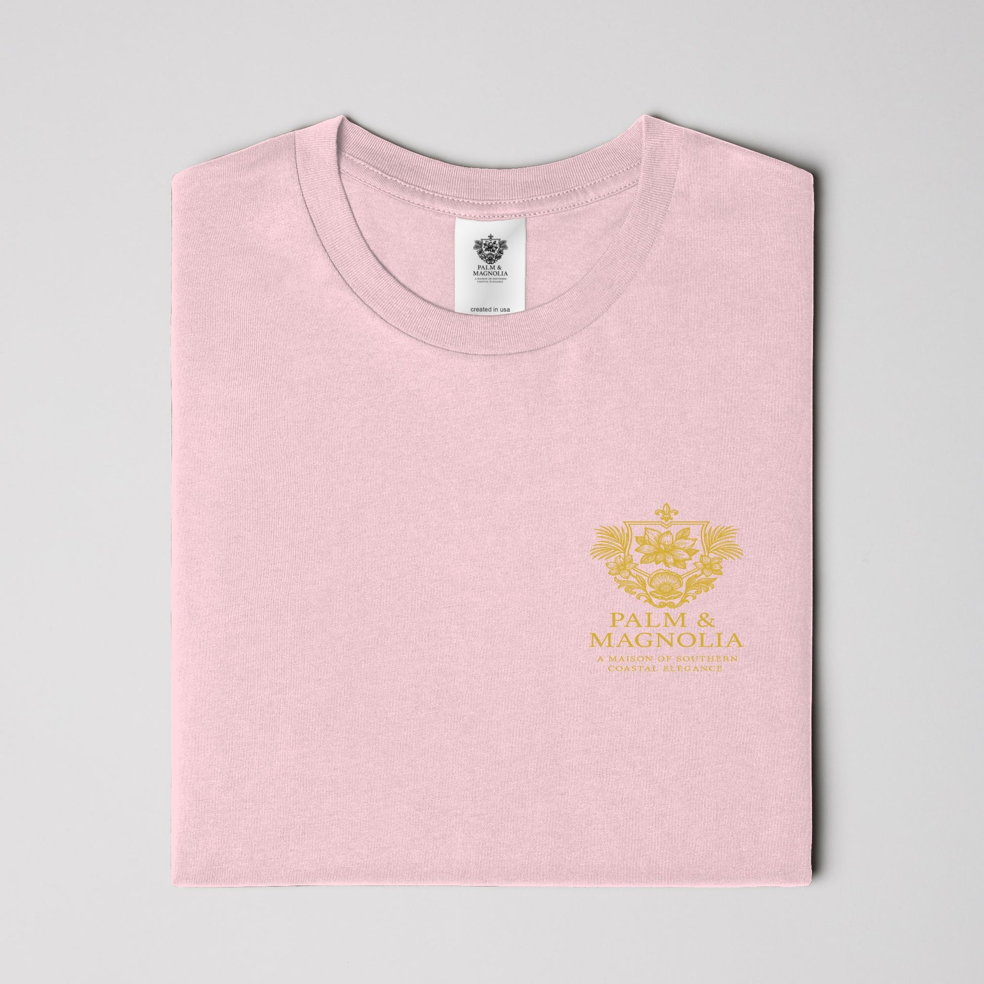 Folded pink unisex tee with gold Palm & Magnolia logo on chest.