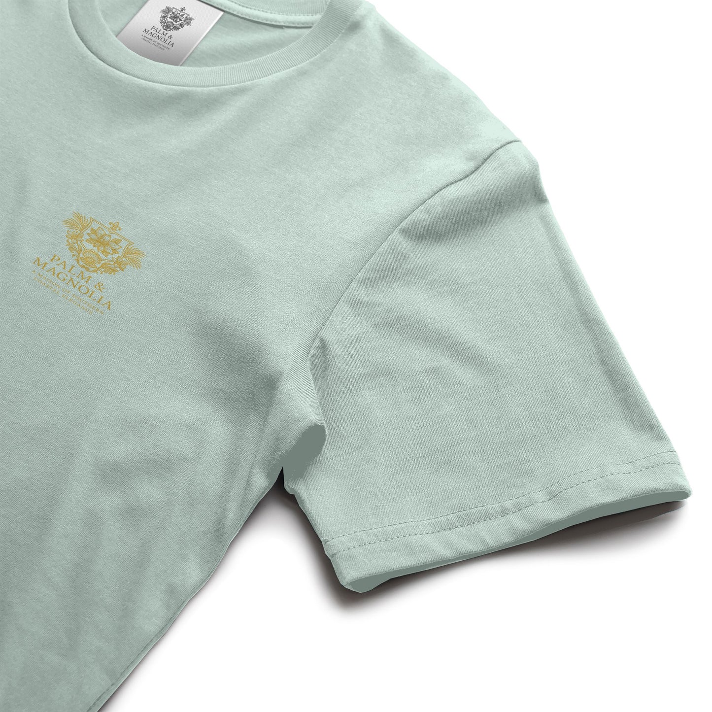 Light green unisex ring-spun cotton tee with gold Palm & Magnolia crest on chest.