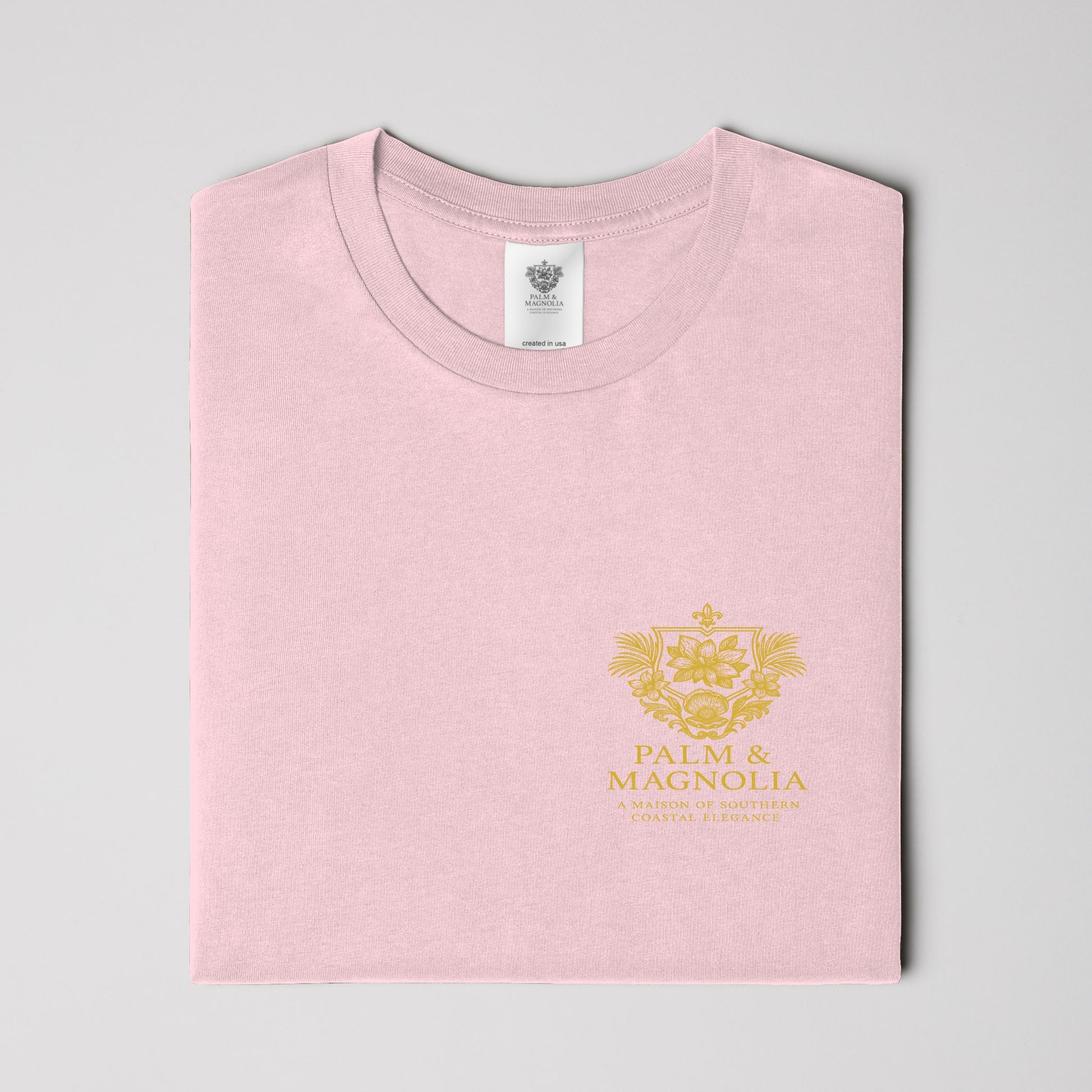 Folded pink ring-spun cotton tee with gold Palm & Magnolia crest.