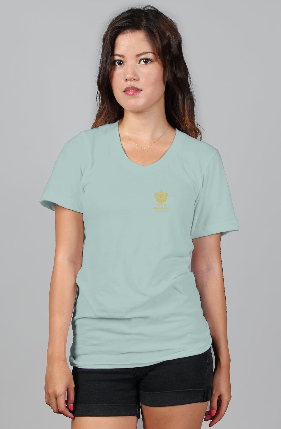 Woman modeling a light blue relaxed-fit V-neck tee with a gold Pascagoula Heritage emblem.