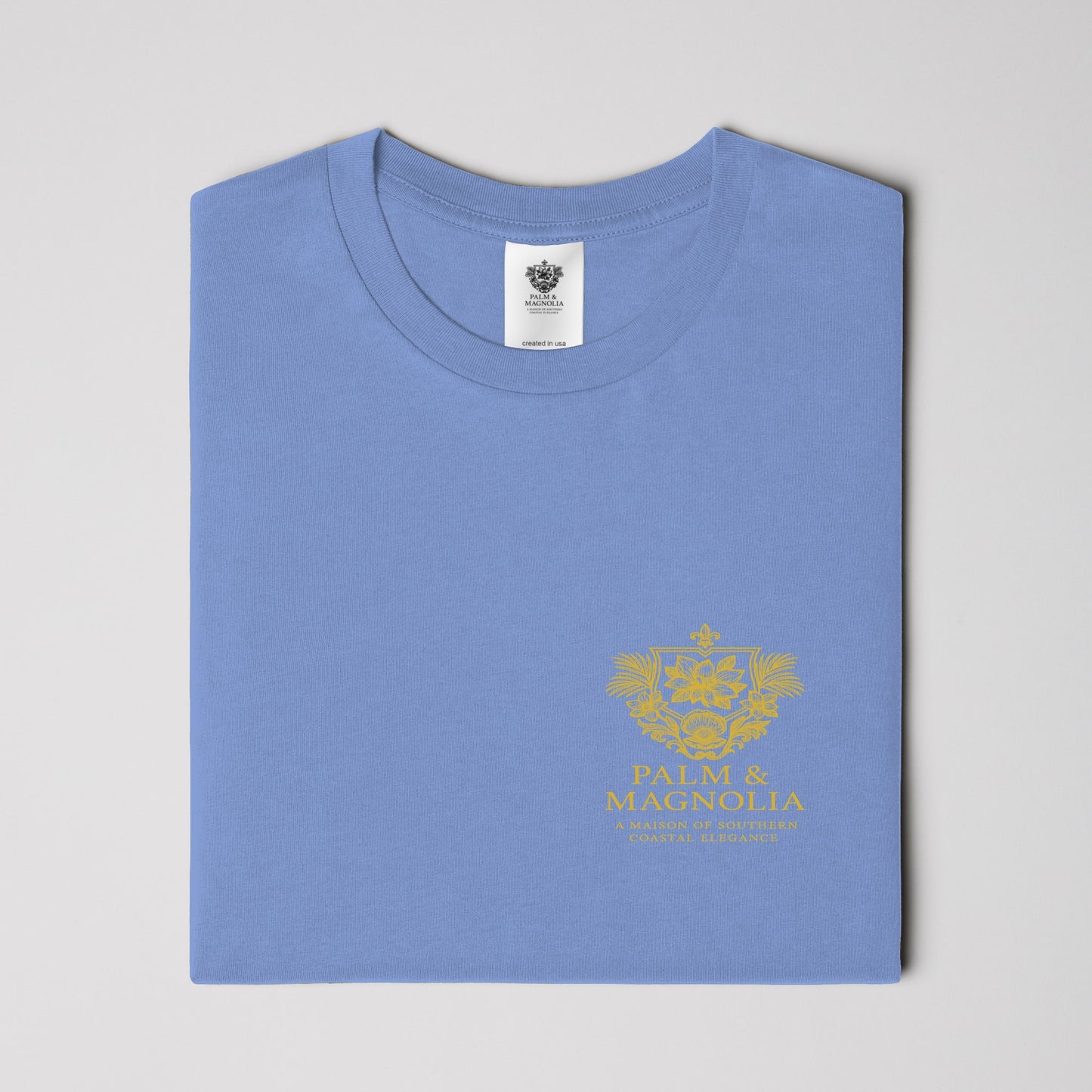 Folded light blue heavyweight Comfort Colors T-shirt with gold Coastal Companions Bayou La Batre logo.
