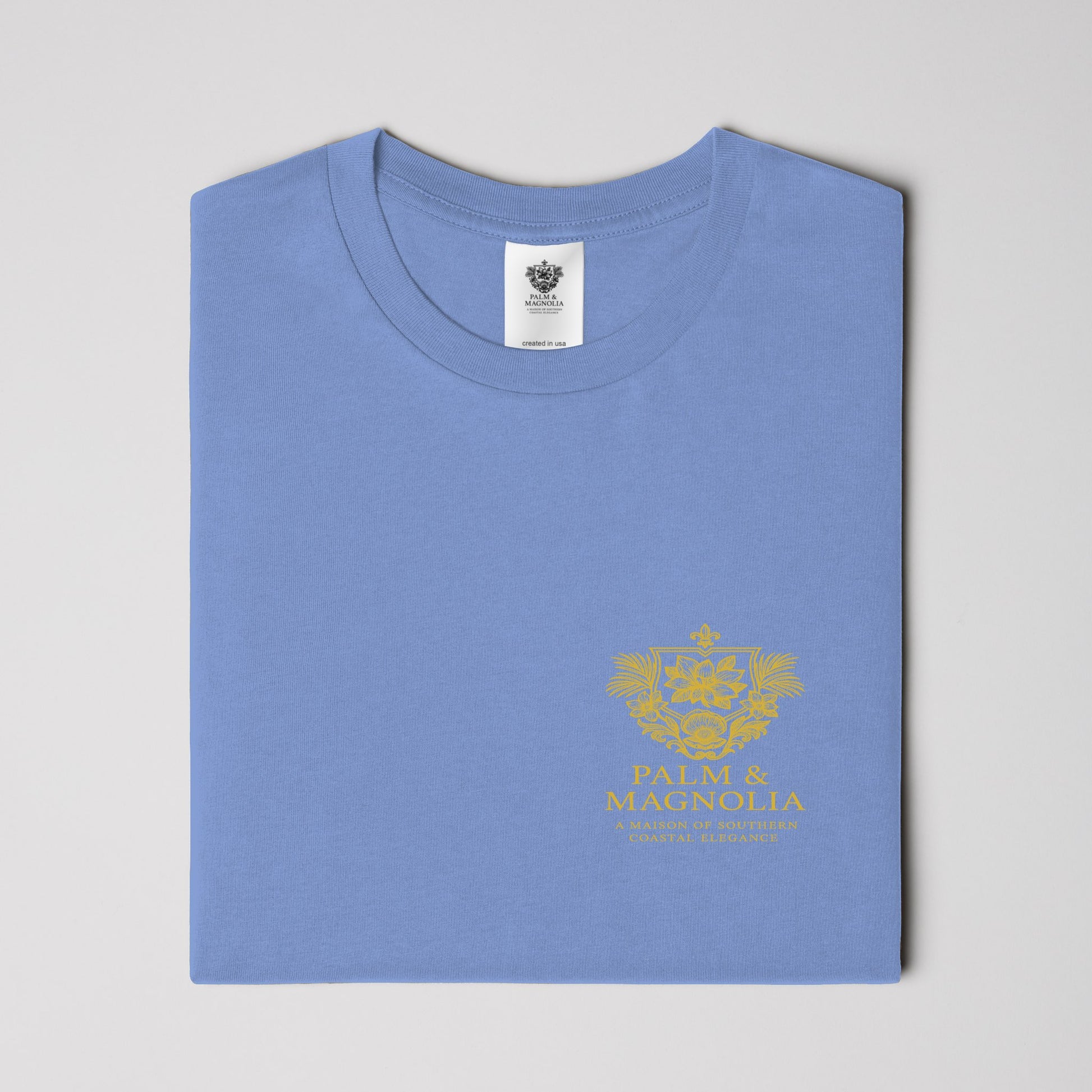 Folded light blue heavyweight Comfort Colors T-shirt with gold Coastal Companions Bayou La Batre logo.