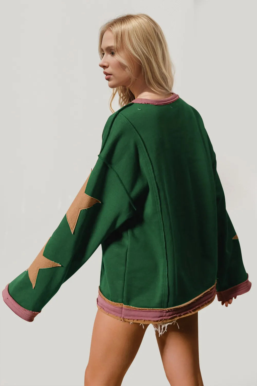 Back view of green long-sleeve sweatshirt with gold star patches on sleeves and pink trim.