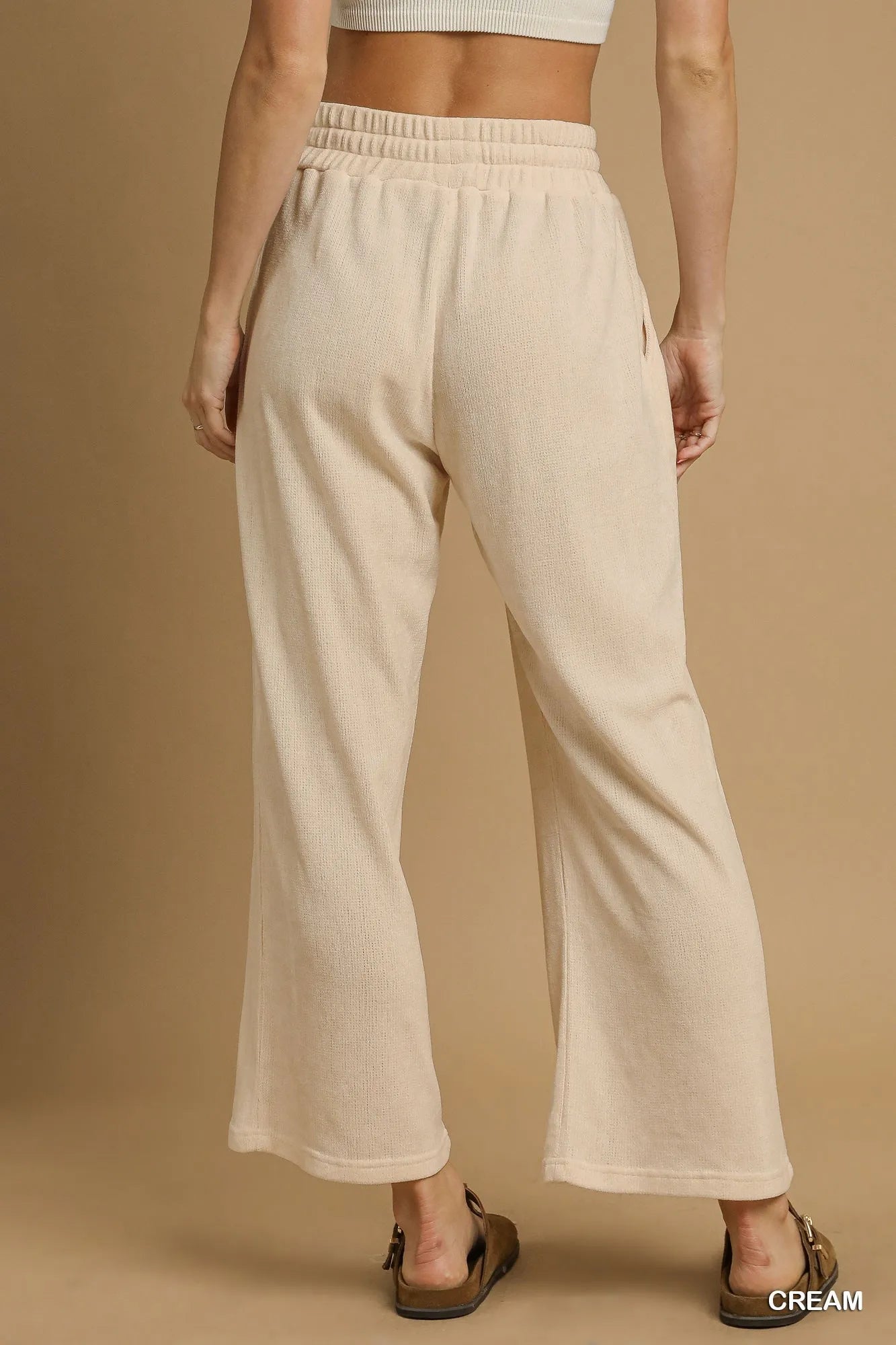 Rear view of cream drawstring wide-leg pants with flowy fit on a model.