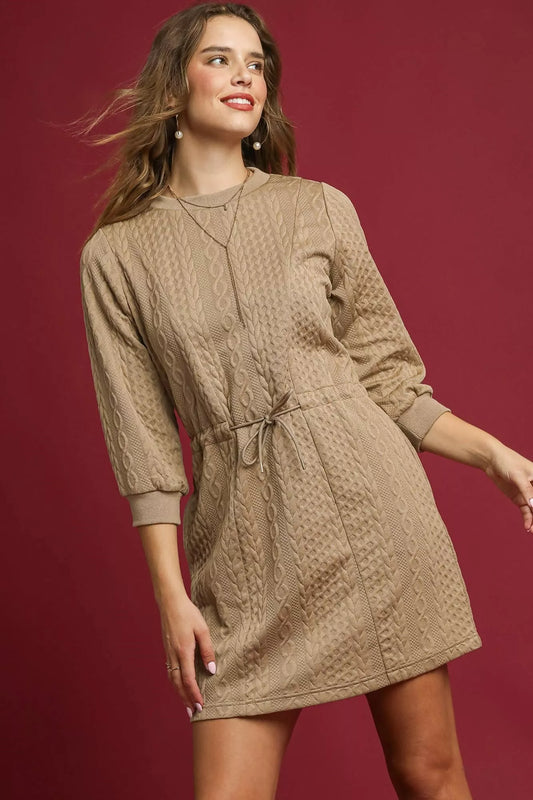 Woman modeling a beige cable knit mini dress with drawstring waist and pockets.