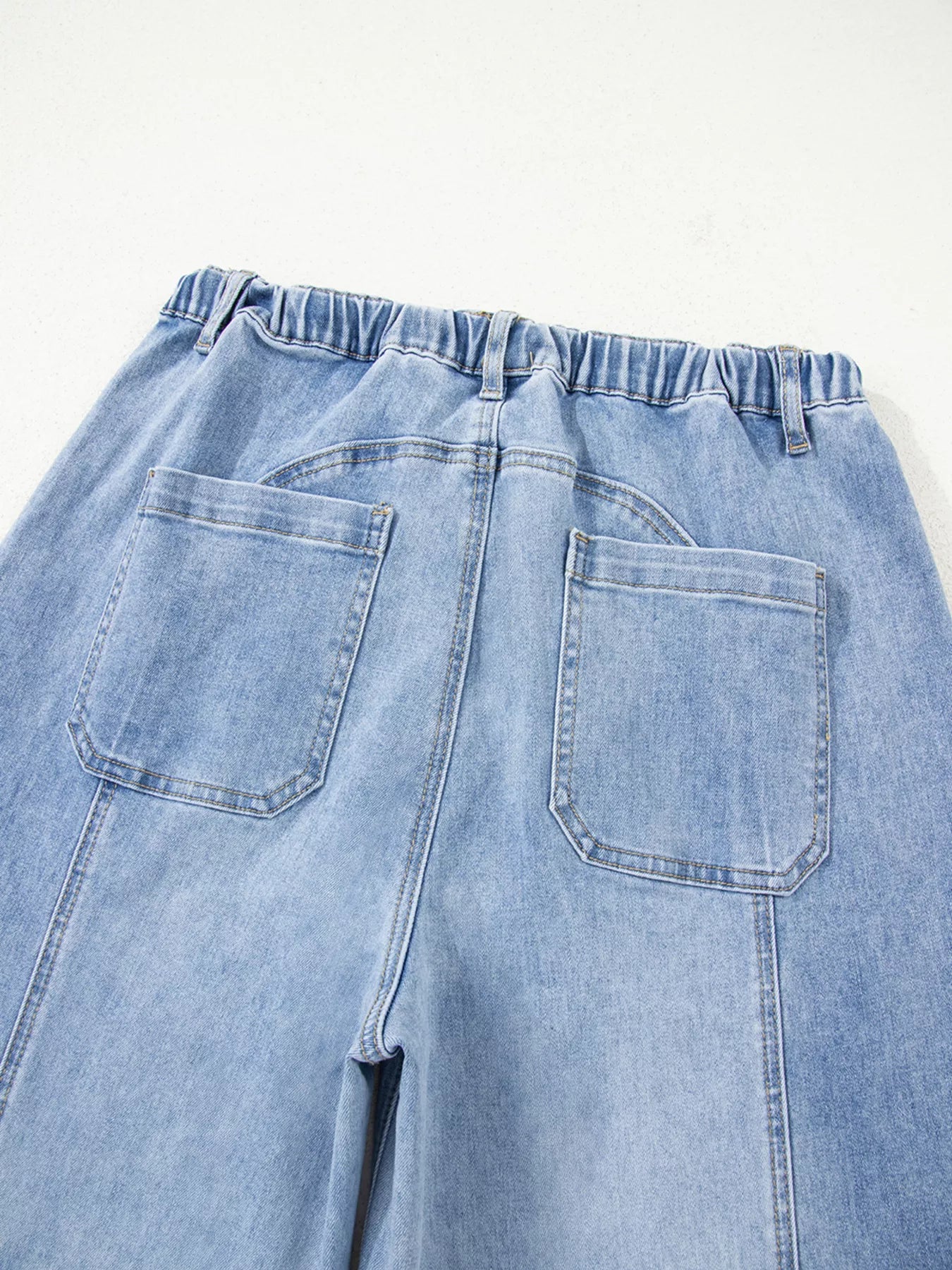 Rear view of light wash wide-leg jeans with drawstring waist, raw hem, and side pockets.