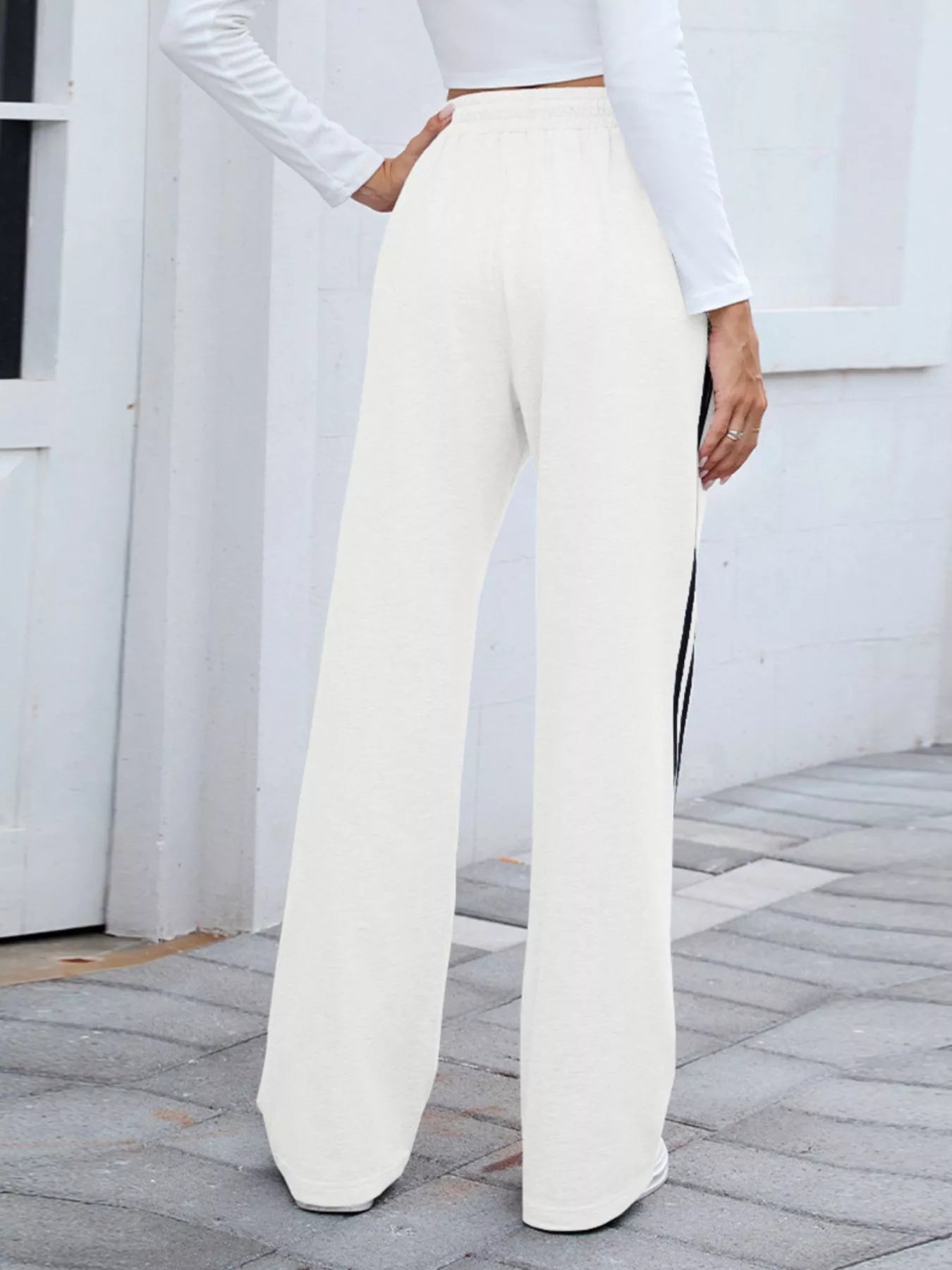 Rear view of white wide-leg pants with black side stripes on a model.