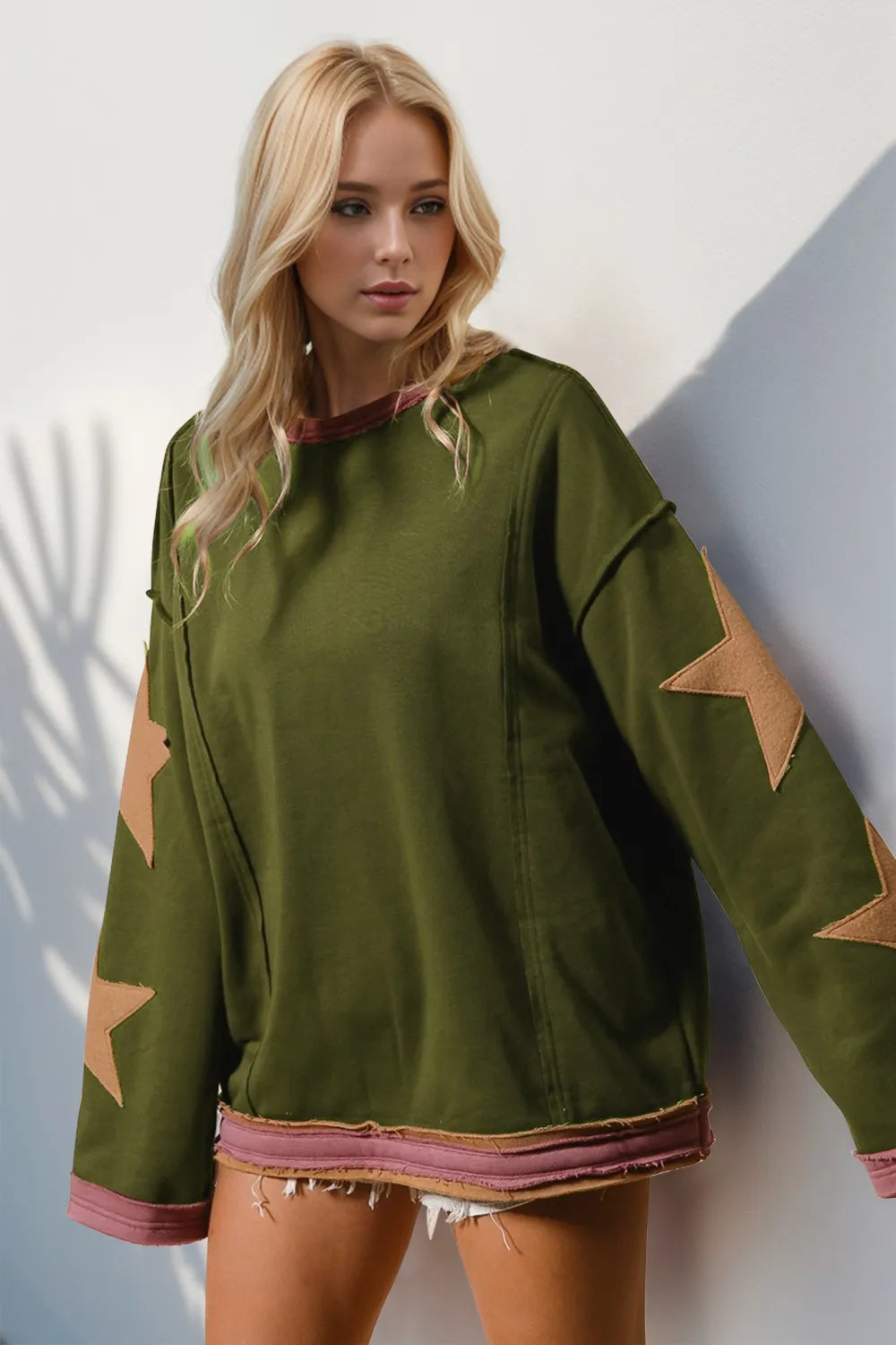 Green long-sleeve sweatshirt with oversized star patches on sleeves and exposed seams.