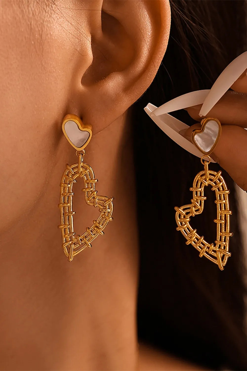 Close-up of a model wearing 18K gold-plated heart earrings with white accents.