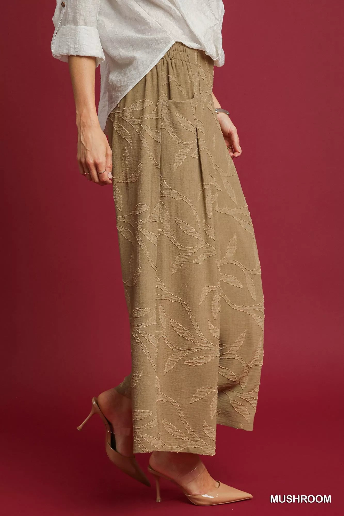 Woman modeling beige jacquard wide-leg pants with leaf patterns, paired with white blouse and nude heels.