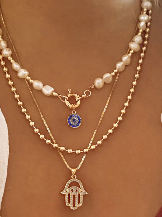 Layered necklace with pearl strands, blue evil eye charm, and gold-plated hamsa pendant.